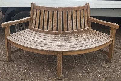 Lot 246 - A teak half tree bench features a gently...